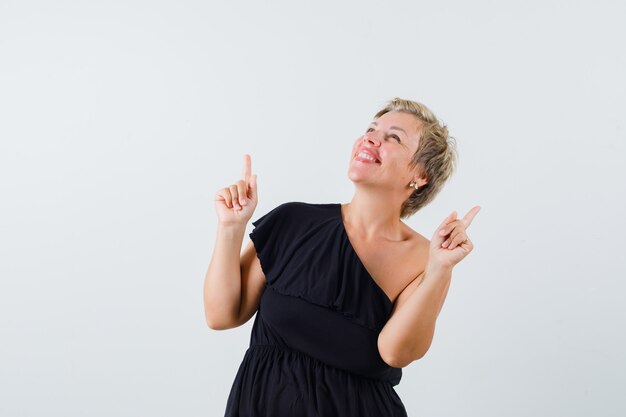 Charming lady pointing up in black blouse and looking happy. front view.