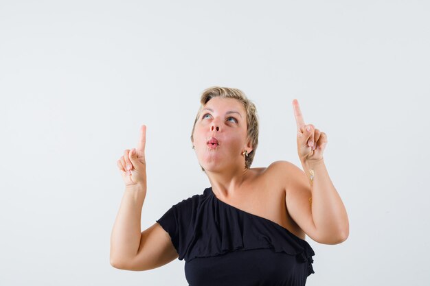 Charming lady pointing up while looking up in black blouse and looking self-confident 