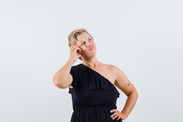 Charming lady posing like making phone call in black blouse and looking thoughtful. front view.