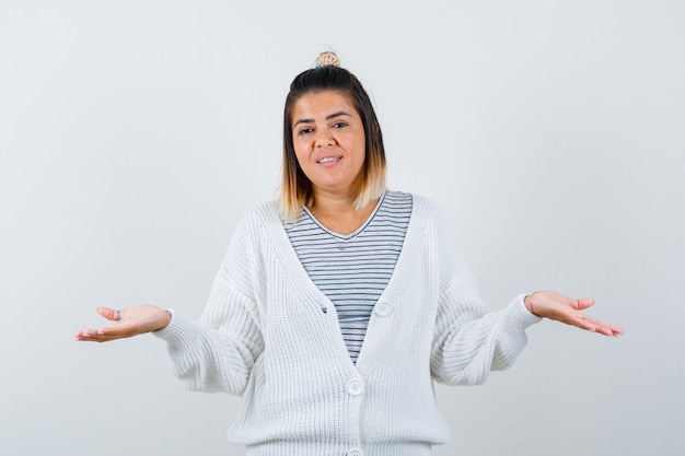 Affascinante signora che mostra gesto impotente in t-shirt, cardigan e sembra allegra.