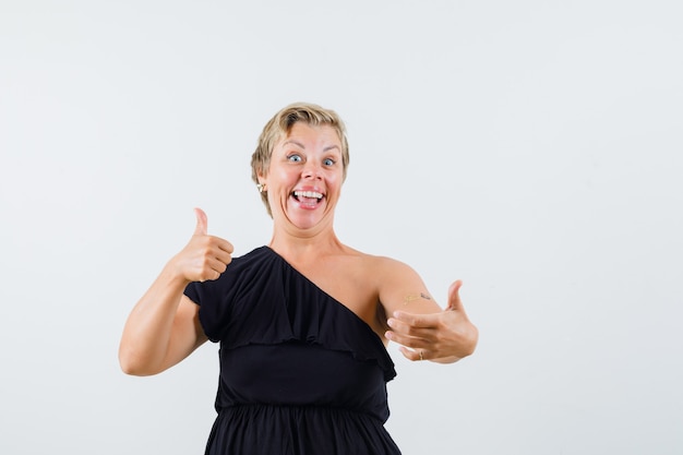 Charming lady showing thumb up while holding phone in black blouse and looking merry 