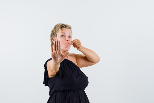 Charming lady showing zip gesture while showing stop gesture in black blouse and looking reluctant. front view.