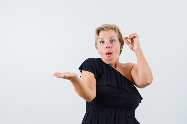 Charming lady spreading her hand while expressing feeling in black blouse front view.