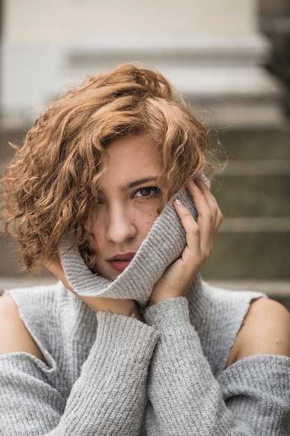 Charming lady with short curly hair holding sweater's collar 