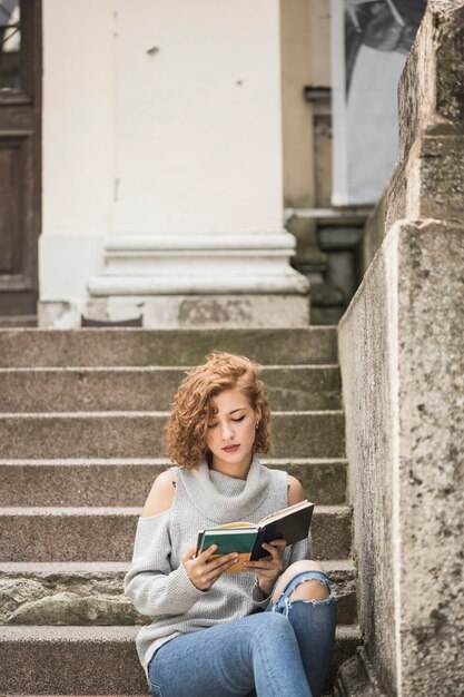 Charming lady with short curly hair reading book