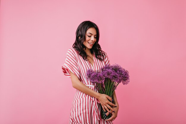 愛情のこもった魅力的なラテン女性は、紫色の野生の花の花束を見ています。縞模様のドレスを着た女の子が恥ずかしいポーズをとる。