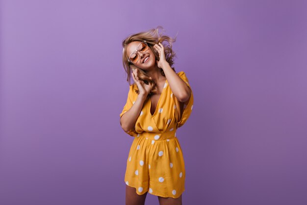 charming laughing woman dancing. debonair tanned girl in orange attire smiling on purple.