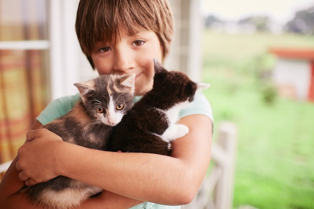 Charming little boy holds two kitties in his arms 