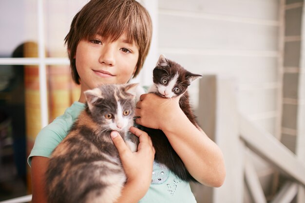 魅力的な小さな男の子は彼の腕の中で2つの子猫を保持します