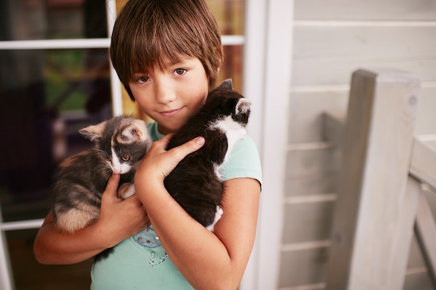 Charming little boy holds two kitties in his arms 