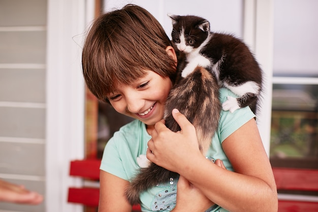 魅力的な小さな男の子は彼の腕の中で2つの子猫を保持します