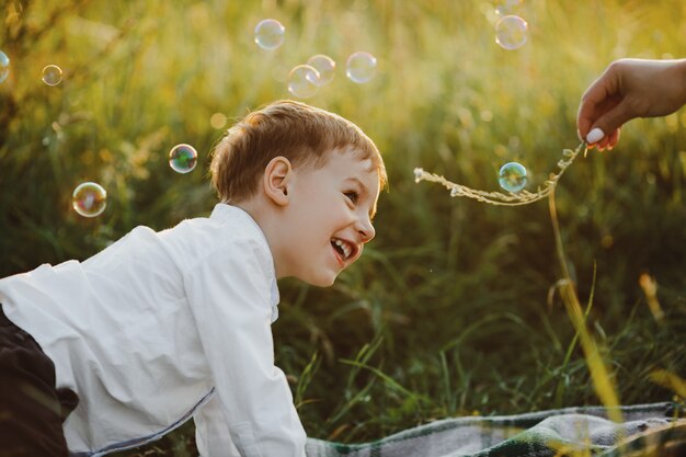 魅力的な小さな男の子は緑の芝生の上にあり、美しいを楽しんでいます