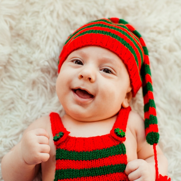 긴 녹색과 빨간 모자에 매력적인 어린 소년은 솜 털 카펫에 놓여