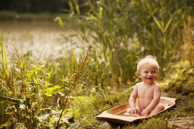 Charming little boy takes a bath on the lawn in green summer park 