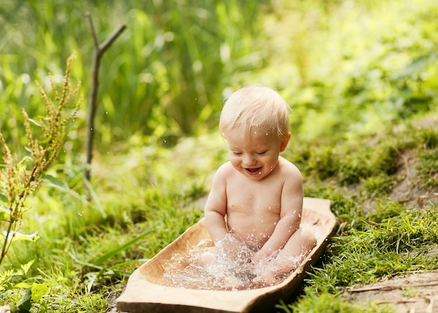 Charming little boy takes a bath on the lawn in green summer park 