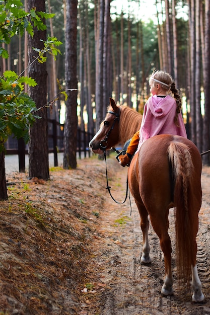 Charming little girl dressed like a princess rides a horse around the autumn forest