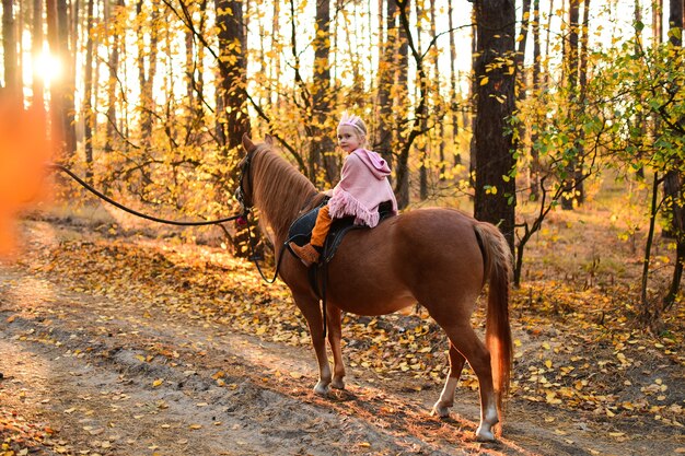 Charming little girl dressed like a princess rides a horse around the autumn forest