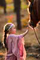 Foto gratuita la bambina affascinante si è vestita come una principessa si leva in piedi con un cavallo nella foresta di autunno