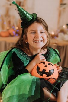 Charming little girl in a green halloween costume of witch or sorceress with a pumpkin lantern jack