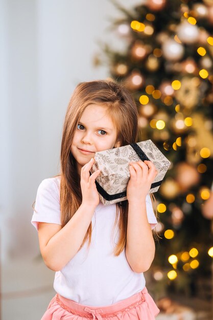 Очаровательная маленькая девочка держит подарок на фоне елки
