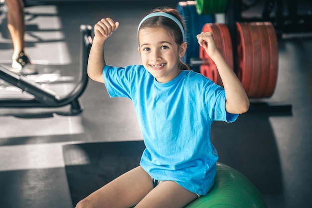 Charming little girl is shows her biceps working out at gym