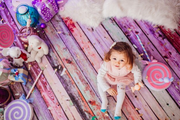 Charming little girl sits on the pink floor among soft toys 