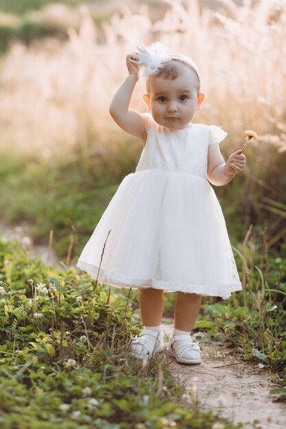 Charming little girl in white dress walks along the path in the field