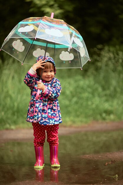 傘を持つ魅力的な少女は、雨の後にプールのガンブートに立って楽しい