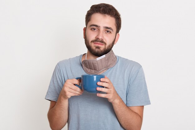 Charming magnetic handsome young bearded man, holding cup with tea in morning, having peaceful facial expression