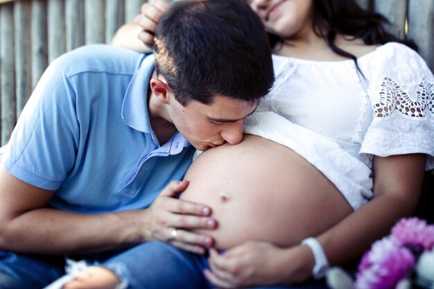 매력적인 남자는 흰 셔츠에 그의 여자의 부드러운 임신 배를 키스