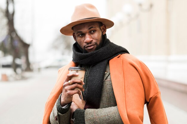 Charming man posing outdoors while holding a cup of coffee