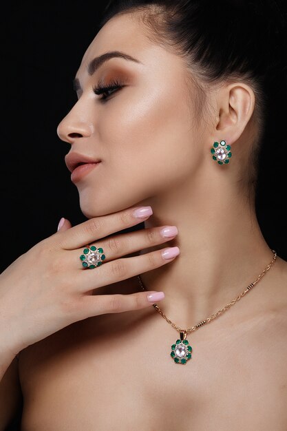 Charming model with dark hair shows rich golden earrings, necklace, and ring 