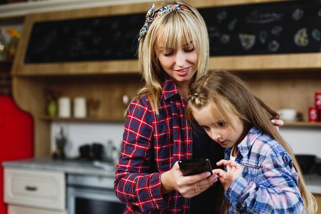 Charming mom and daughter in the same t-shirts look at something in a smartphone 