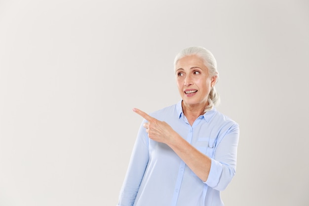 Charming old lady with silver hair, pointing with finger, looking aside