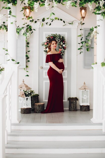 Charming pregnant woman in marsala dress posing on steps of house