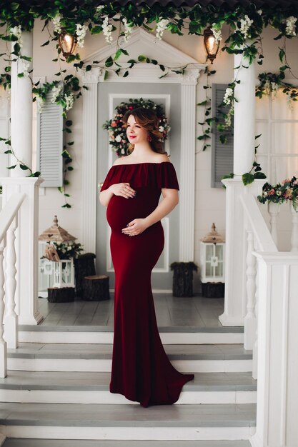 Charming pregnant woman in marsala dress posing on steps of house