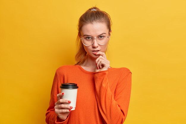 매력적인 심각한 백인 여자는 카메라에 진지하게 보이는 커피를 마신다