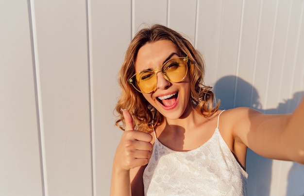 Free photo charming smiling girl in yellow eyeglasses winking and showing a thumb up