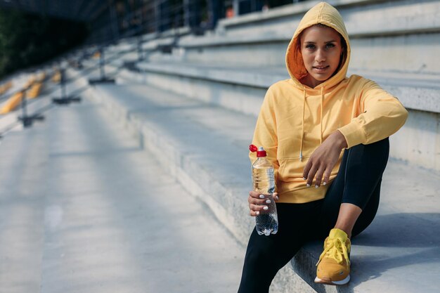 Charming sportswoman sitting on steps and looking at camera