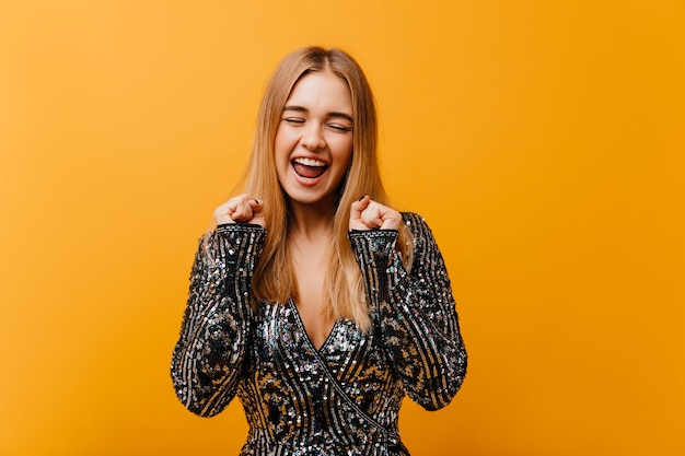 Affascinante donna elegante che esprime felicità e sorridente. bella donna positiva in giacca scintillante in piedi sull'arancio