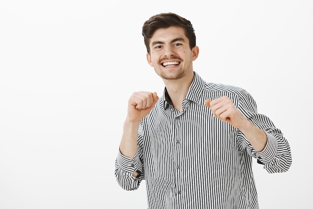 Charming successful office manager, celebrating good deal with special dance. Portrait of pleased joyful european man with moustache, raising hands and making dance moves while in club with mates