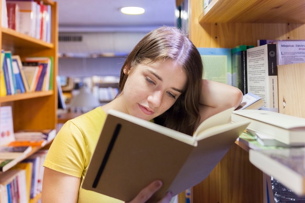 Очаровательное чтение подростка между книжными шкафами