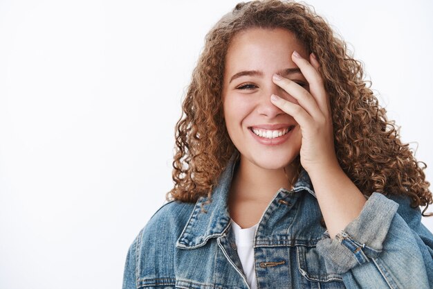 Charming upbeat optimstic dreamy curly-haired plump girl smiling white teeth blushing flirty hide half face palm have fun laughing cute, studio wall