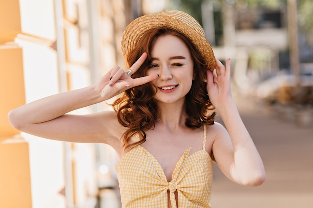 夏の幸せを表現するヴィンテージドレスの魅力的な白人女性。街で笑っている帽子をかぶったファッショナブルな生姜の女性の屋外写真。
