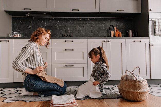 Очаровательная женщина и ее дочь сидят на кухне и кладут вымытый тир