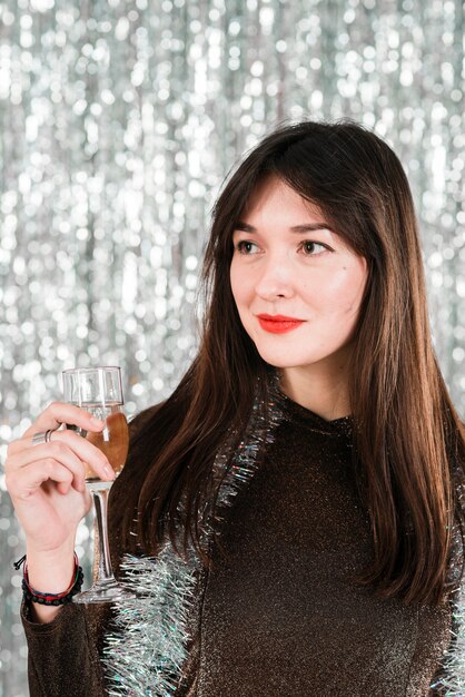 Charming woman holding glass near tinsel 