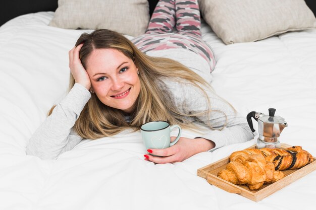 Charming woman lying on bed near breakfast food