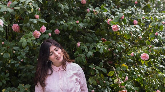 Очаровательная женщина возле многих розовых цветов, растущих на зеленых веточек