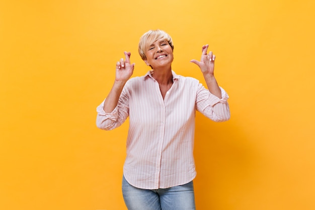 Charming woman in plaid shirt crosses fingers on orange background