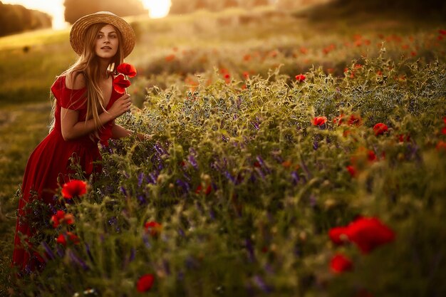 Charming woman walks across a green field with poppies in the rays of evening sun